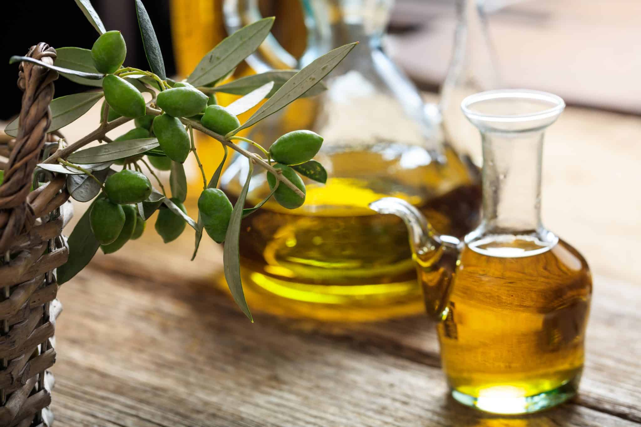 Olive oil and olive twig on a wooden table next to a basket.