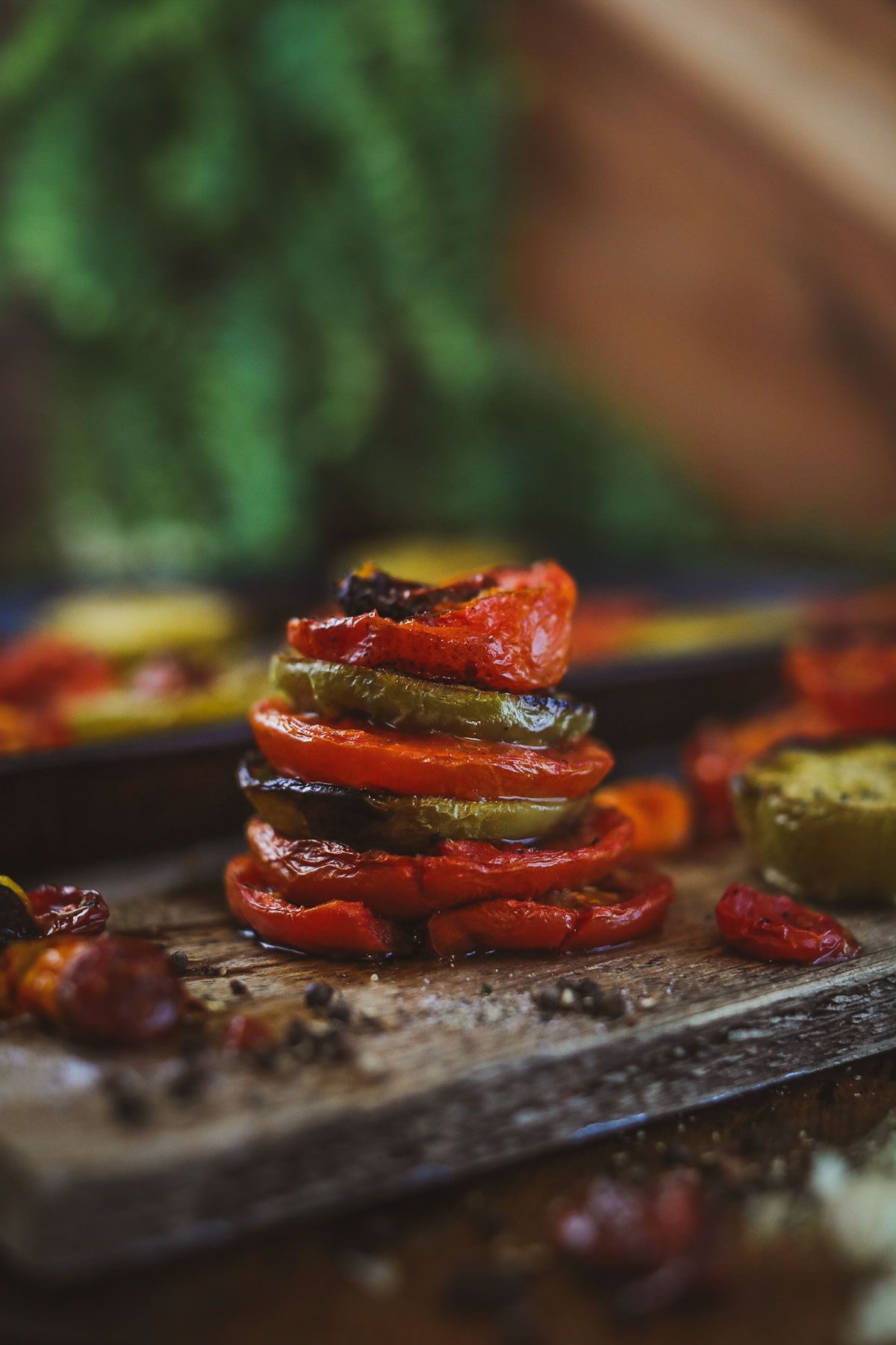 Smoked tomatoes stacked vertically on a wooden cutting board.