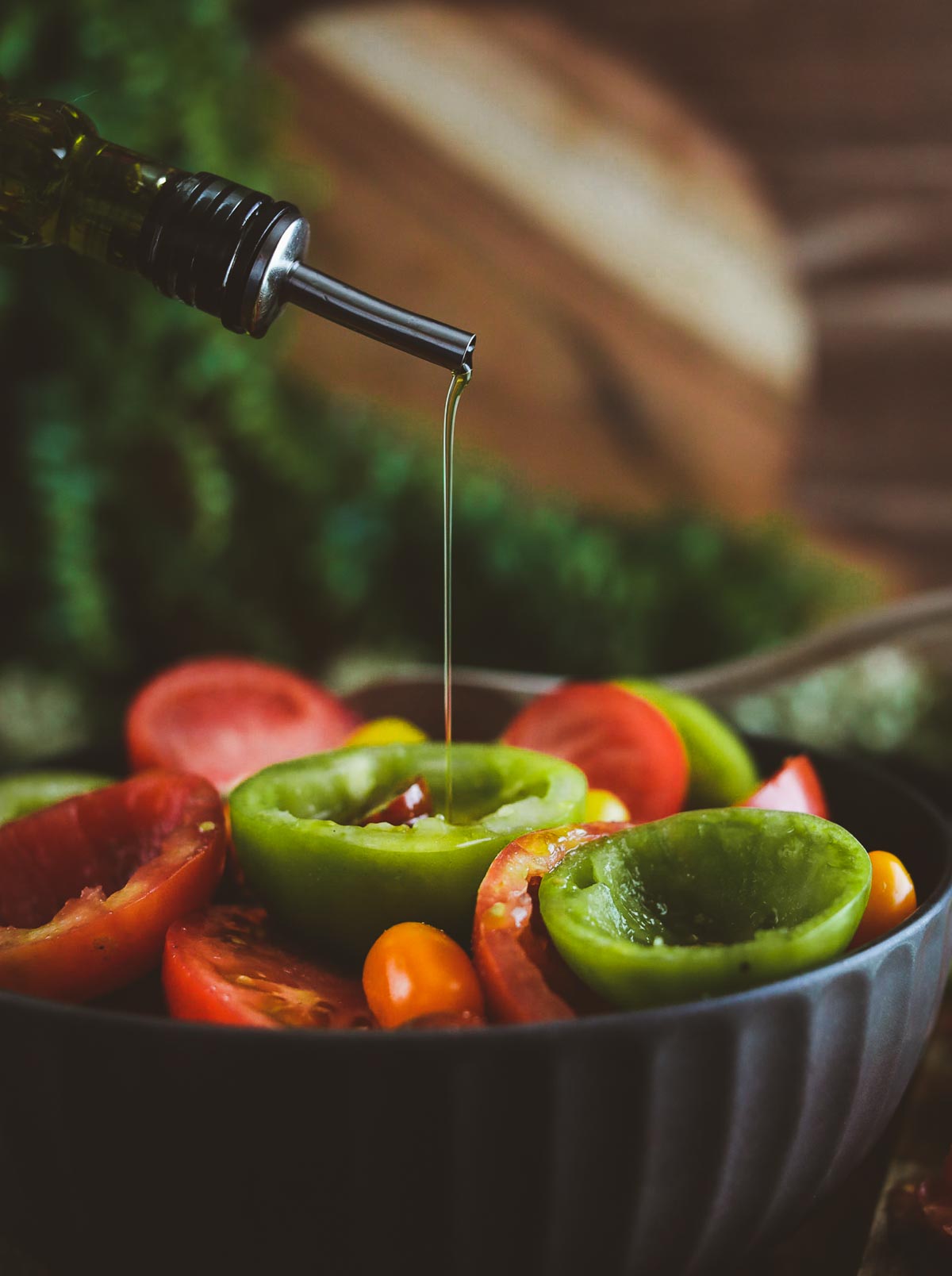 Olive oil being poured over tomatoes in bowl.