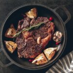 A pan seared and butter basted ribeye steak on a heavy cast iron skillet full of aromatics.