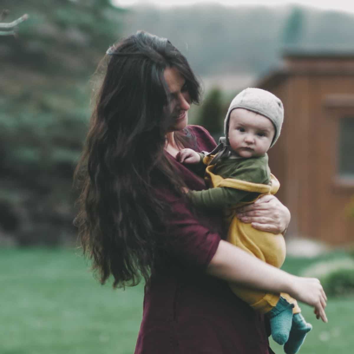 A woman with long dark hair wearing a dress is holding a baby boy.