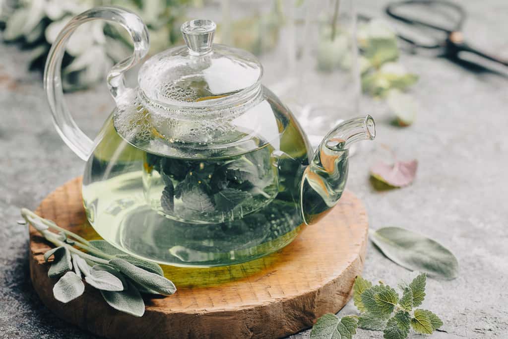 a glass teapot full of mint leaves on a wooden circle stand.