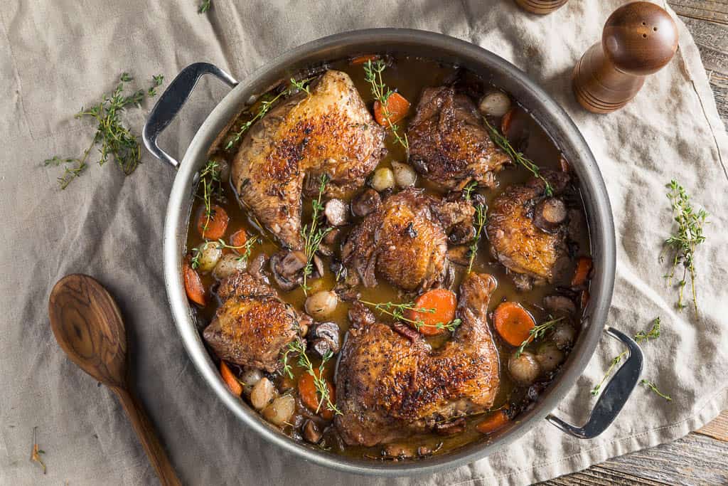 a pot of coq au vin chicken stew on a linen table cloth