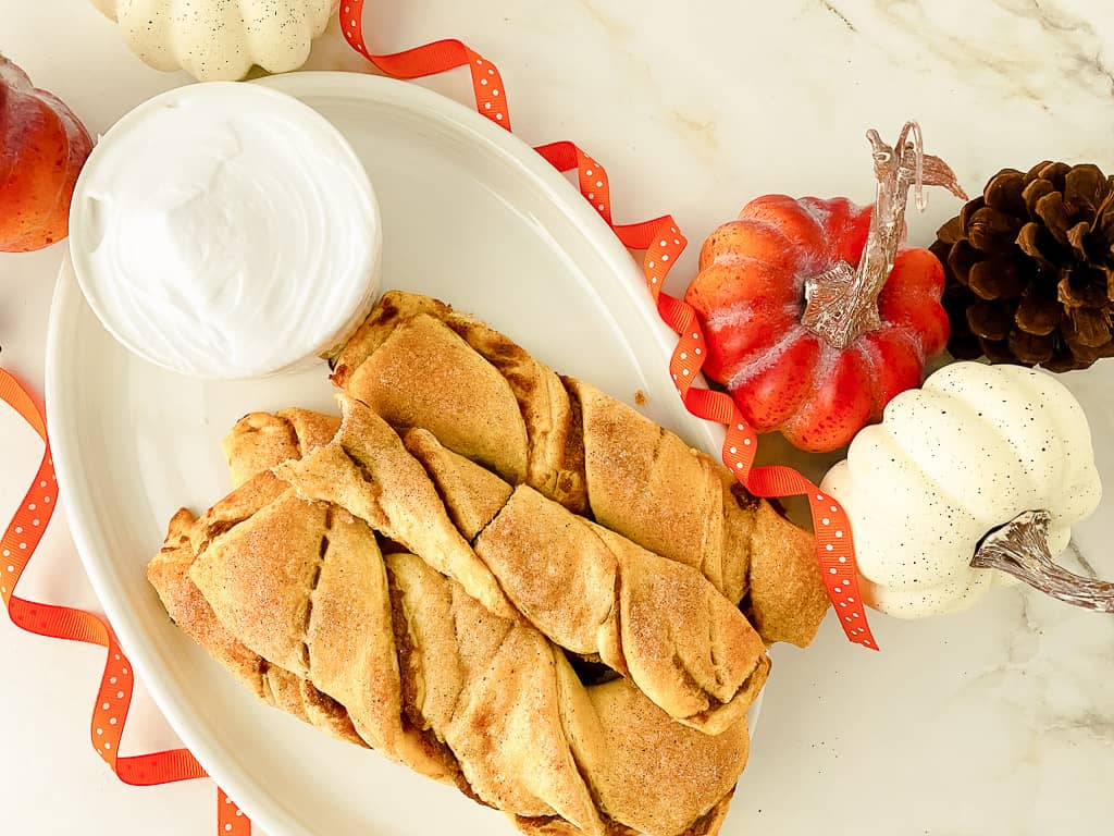 pumpkin pie twists on a white plate with cream cheese frosting in small bowl