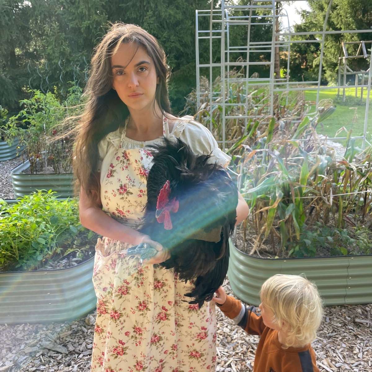 A photo of me and my son in my vegetable garden as I hold a huge, black, Orpington rooster.