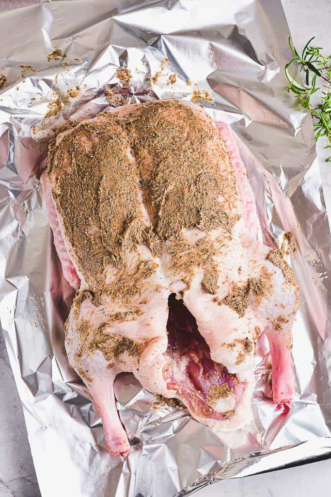 whole raw duck on foil paper. The duck is covered with a thick paste of butter and spice.