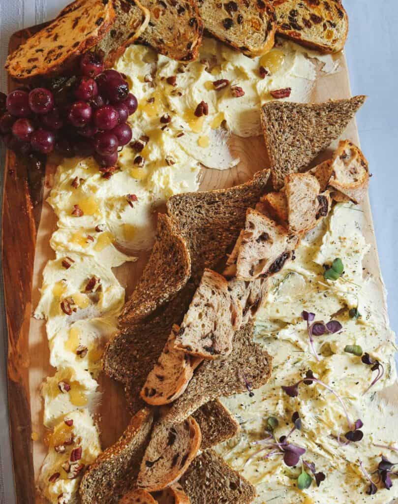 a sweet and savory butter board with an assortment of breads, roasted grapes.