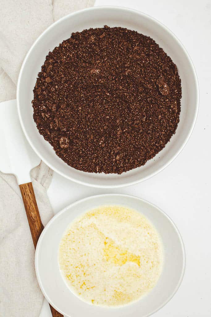 A bowl of melted butter next to a bowl of cookie crumbs.