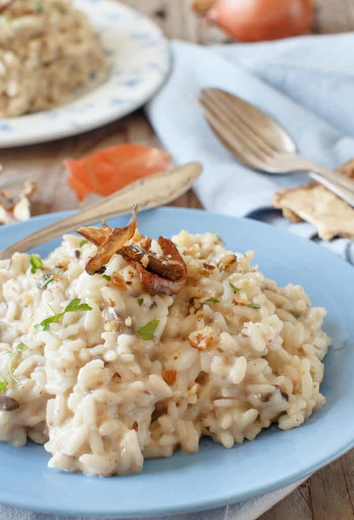perfectly cooked risotto topped with porcini mushrooms on top of a blue and white plate. There is a fork inside of it.