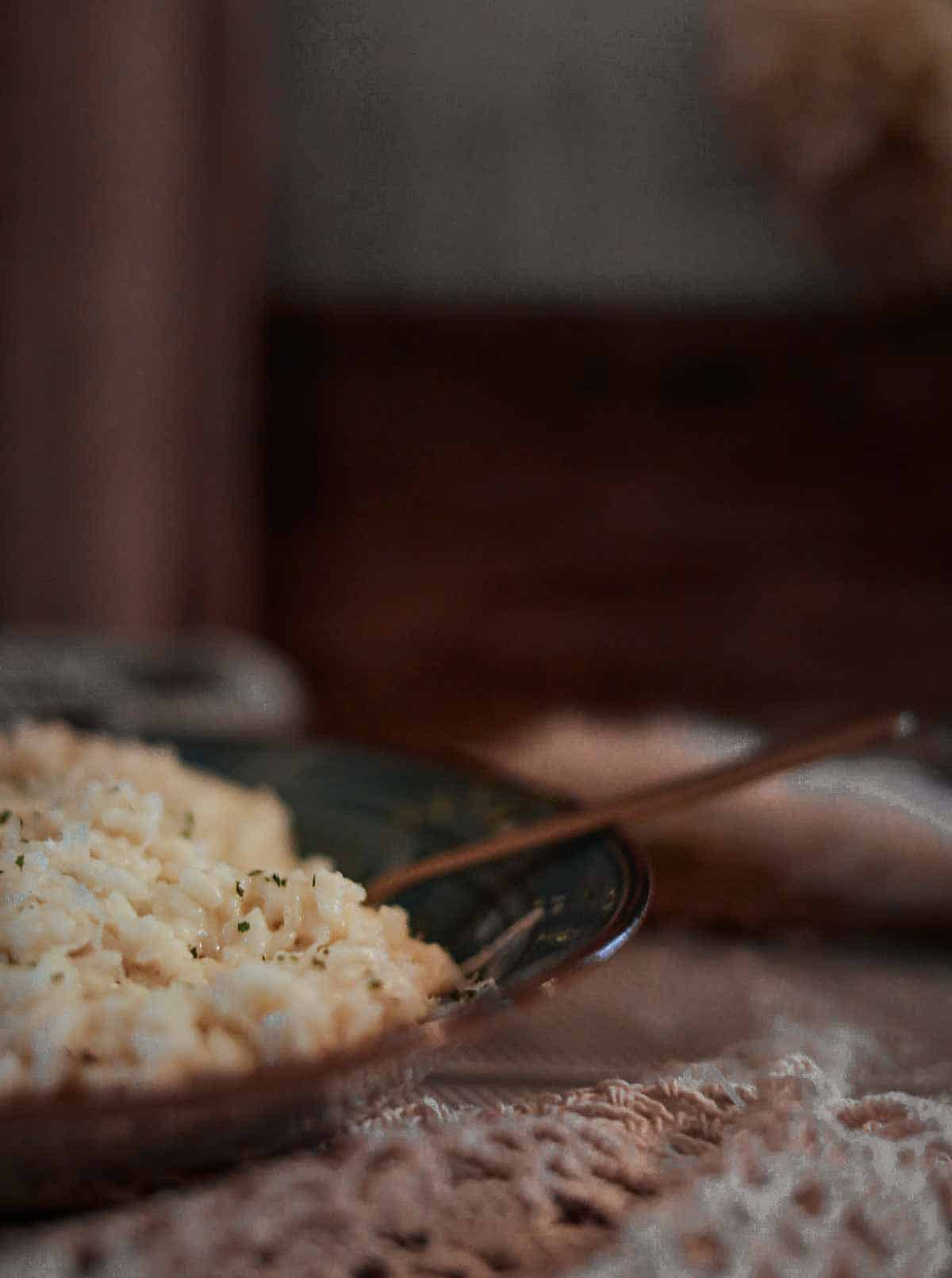 A blue plate full of finished, creamy, perfect risotto. A sideways picture with a spoon inside the dish.