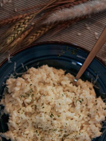 A blue plate full of finished, creamy, perfect risotto. There is a spoon in it.