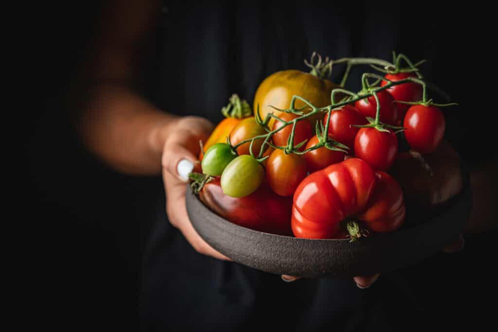 a woman's hands holding a bowl of assorted heritage tomatoes