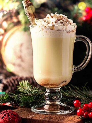 a tall glass of traditional aged eggnog topped with whipped cream and grated nutmeg.
