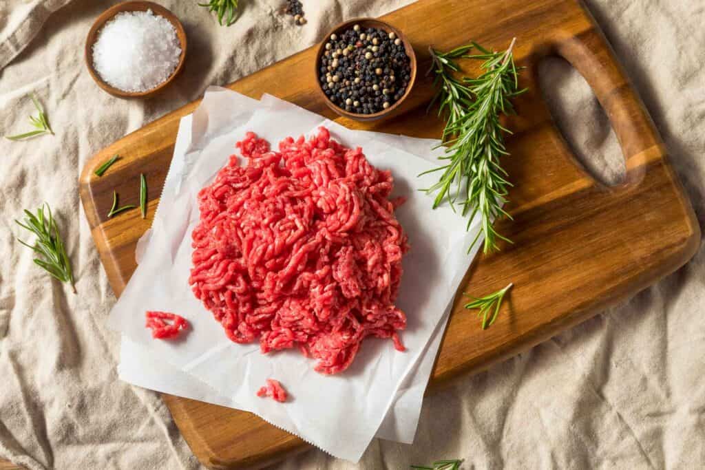 Raw ground beef on a wooden cutting board on a linen table cloth.
