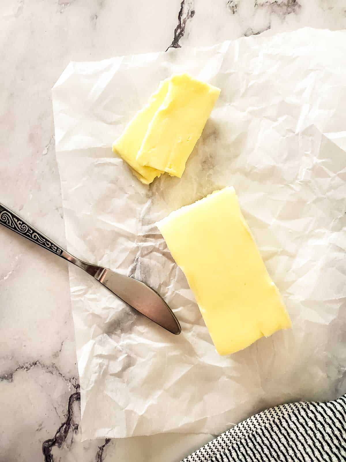 A rectangular block of homemade cultured butter on a crumpled piece of parchment paper next to a silver knife.