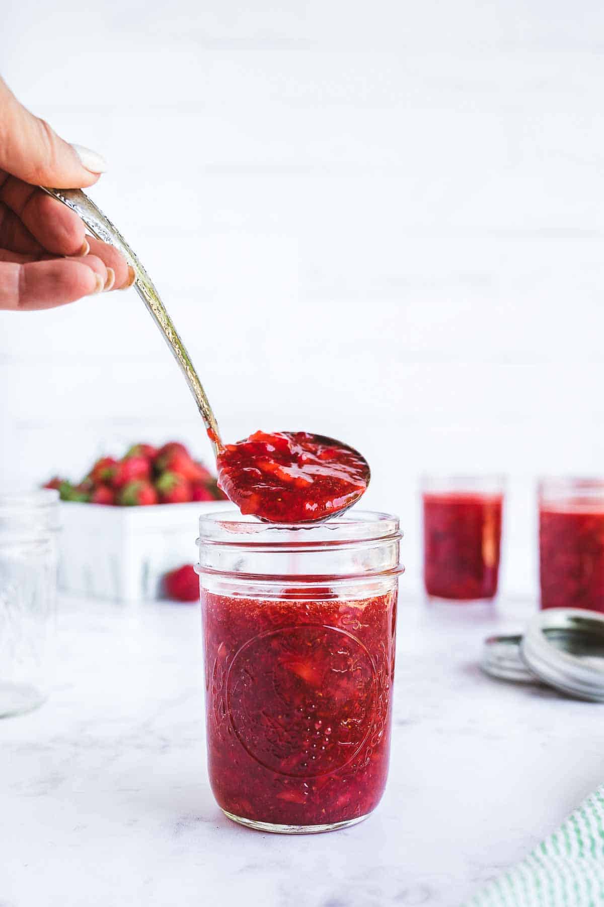 Strawberry freezer jam being ladled into mason jars for freezing.