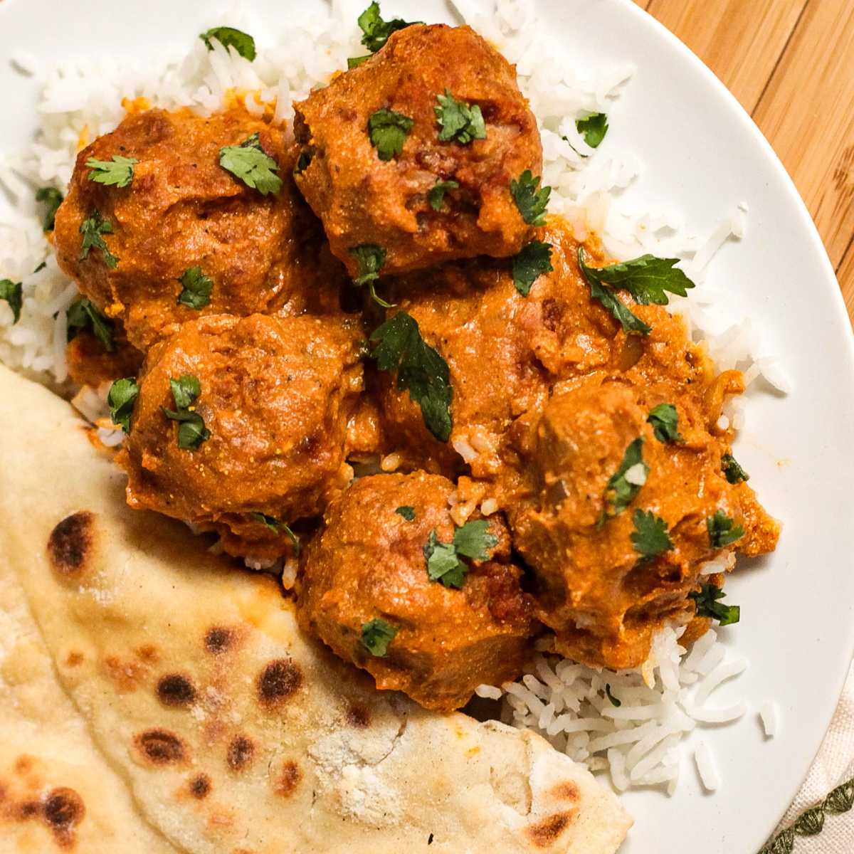 Butter chicken meatballs in a homemade butter sauce on a plate of basmati rice with naan bread on the side.