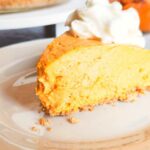 A big slice of no-bake pumpkin cheesecake with a dollop of fresh whipped cream on top is served on a white plate.