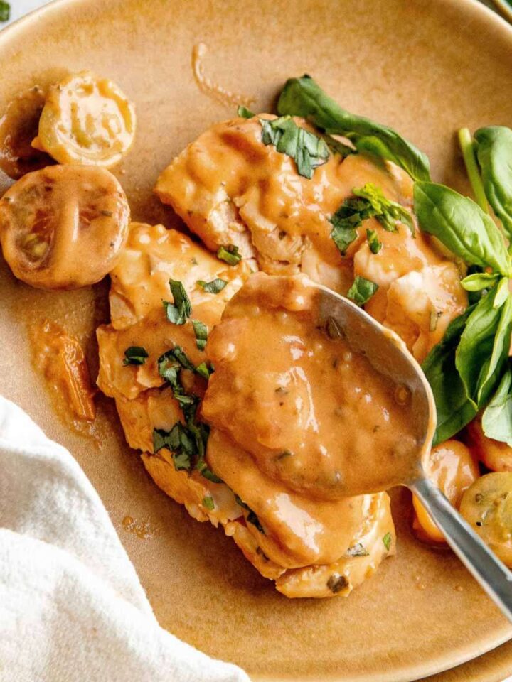 Creamy, crock pot chicken breasts on a light brown plate. They are smothered in extra sauce.