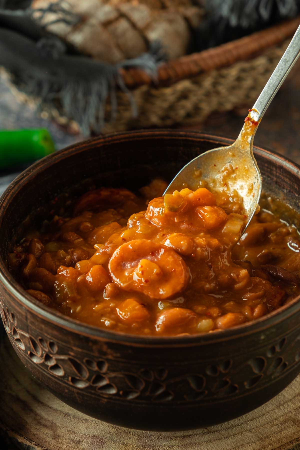 A large bowl full of Bosnian bean soup grah with a spoon in it. The soup is very thick and full of beans and other vegetables.