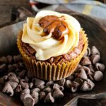 A chocolate brownie buckeye cupcake frosted with peanut butter frosting and a dollop of chocolate. It's sitting on a dark wood pumpkin-shaped platter.