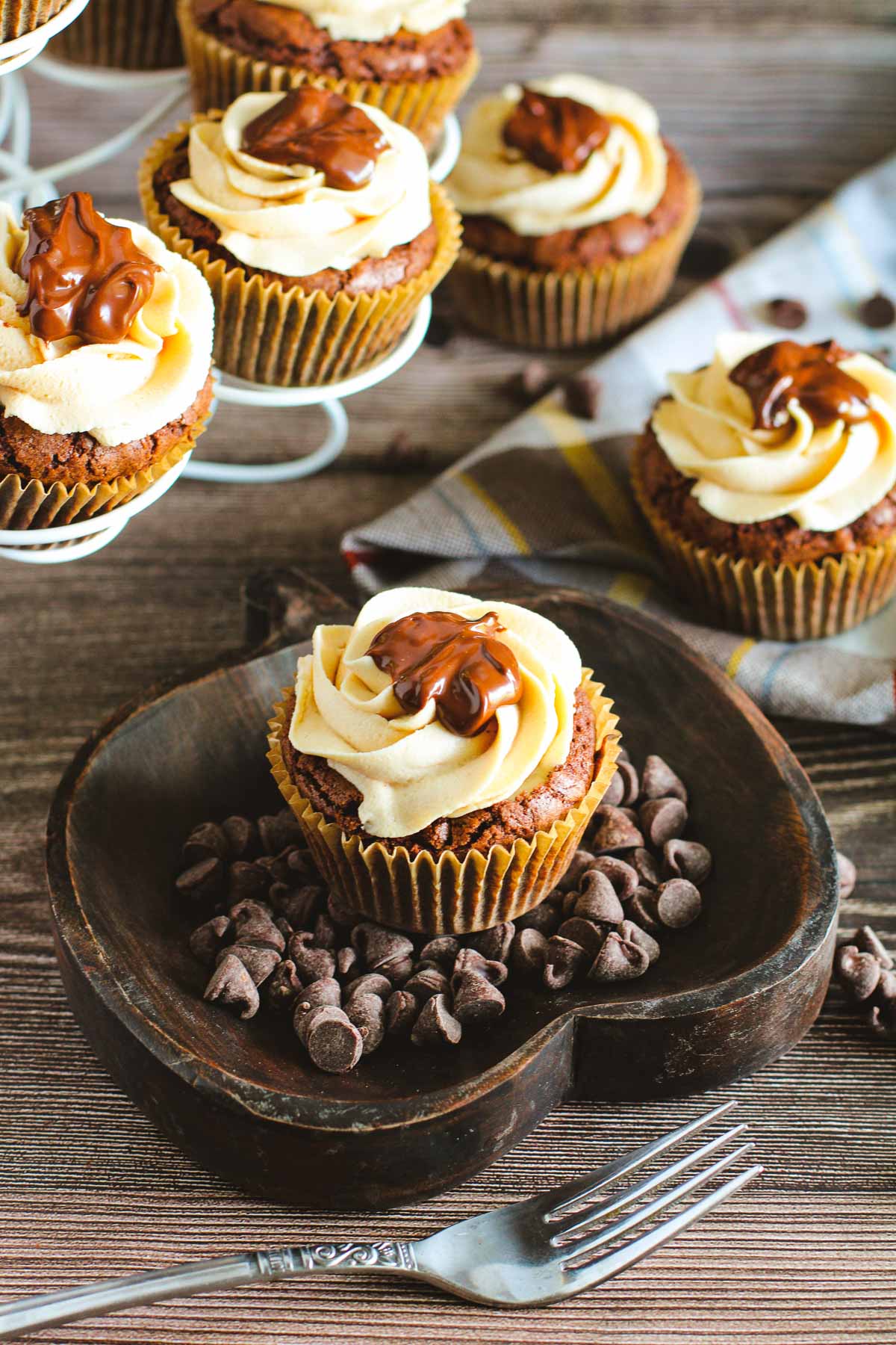 A chocolate brownie buckeye cupcake frosted with peanut butter frosting and a dollop of chocolate. It's sitting on a dark wood pumpkin-shaped platter.