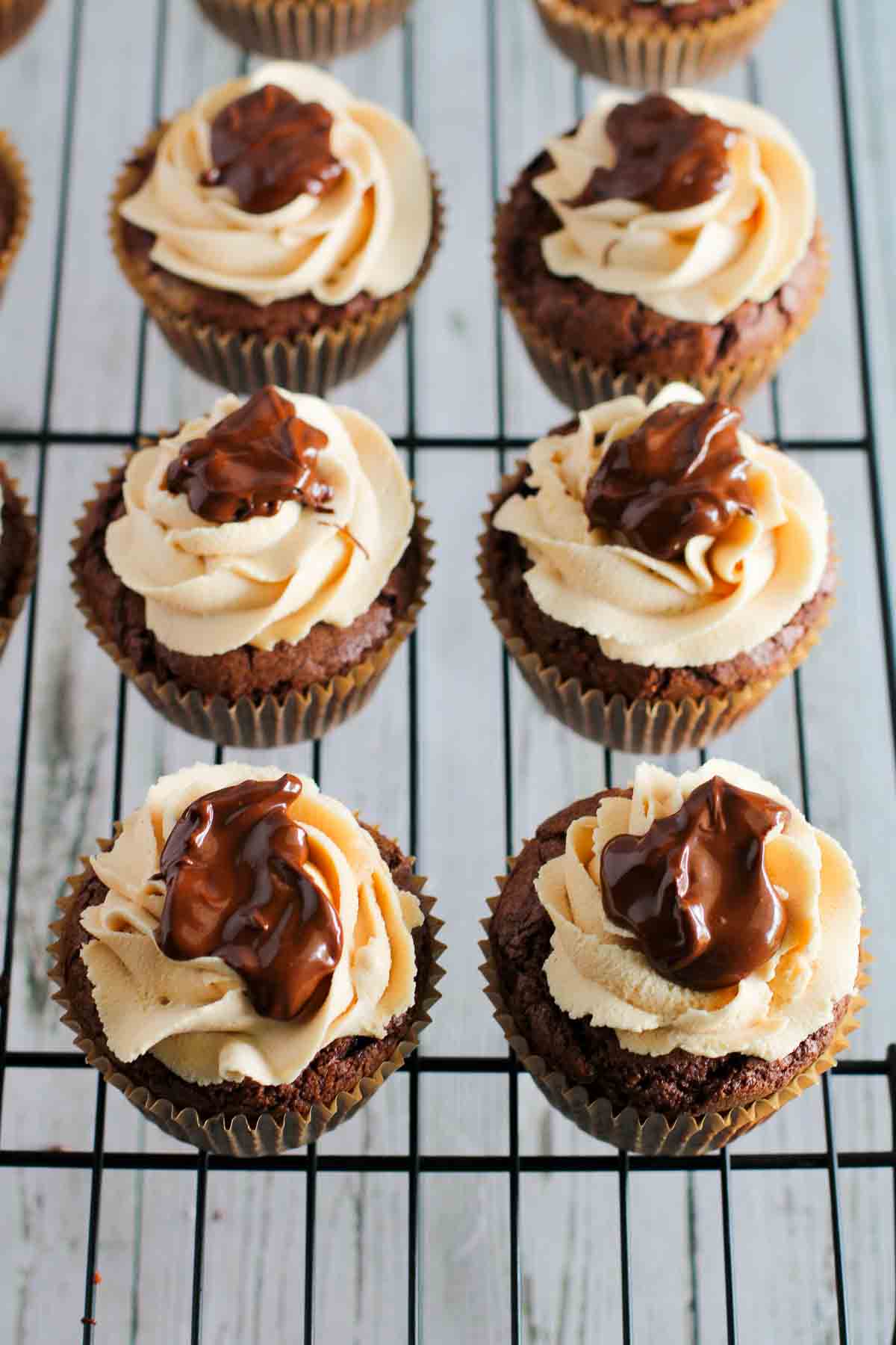 A rack of cupcakes fully frosted with melted chocolate topping drizzled onto the top.