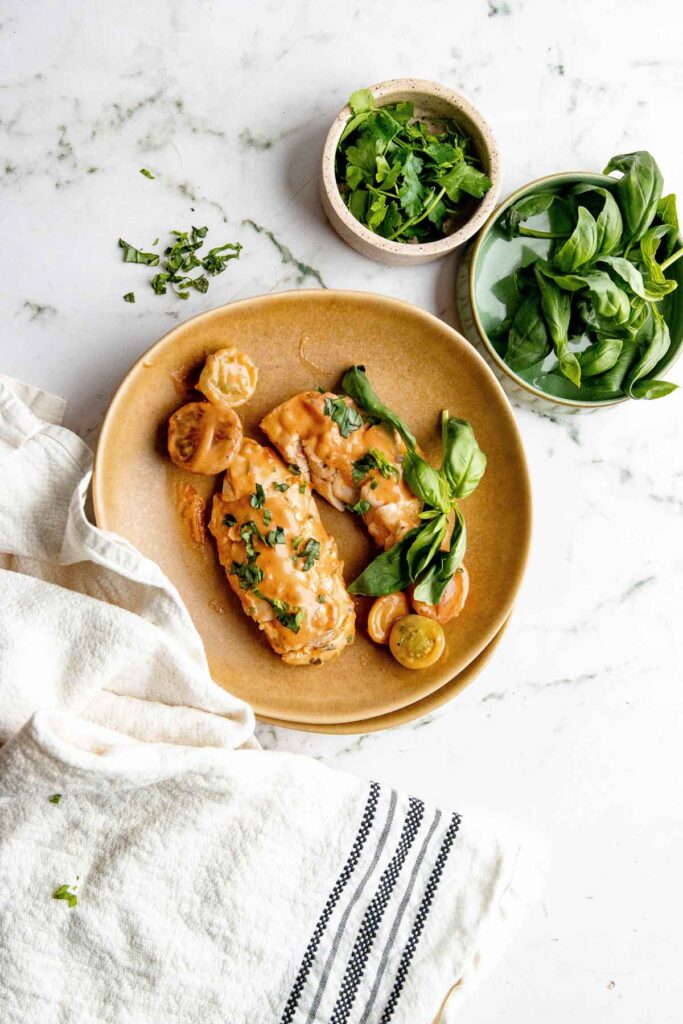 Creamy, crock pot chicken breasts on a light brown plate. They are smothered in extra sauce.