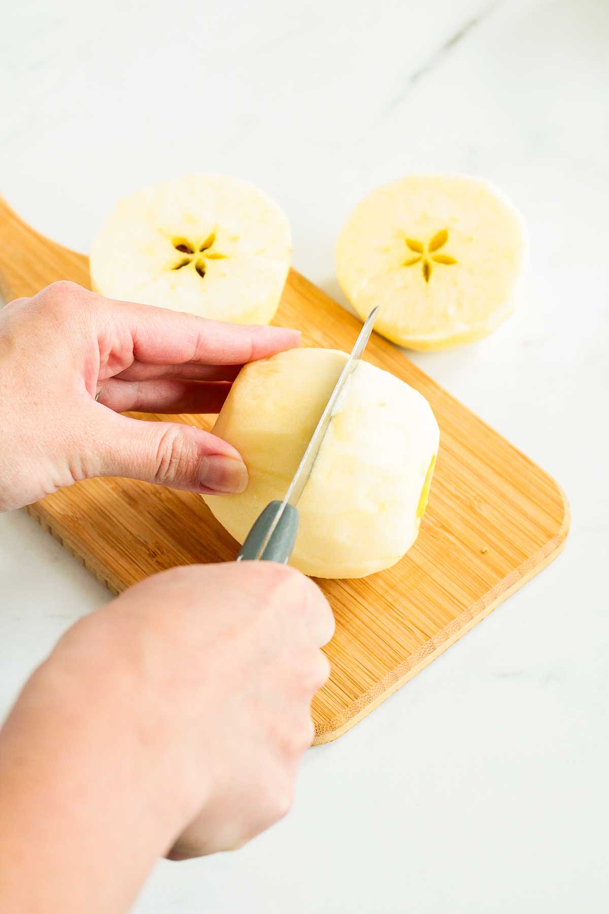A peeled white-fleshed apple being sliced on a cutting board.