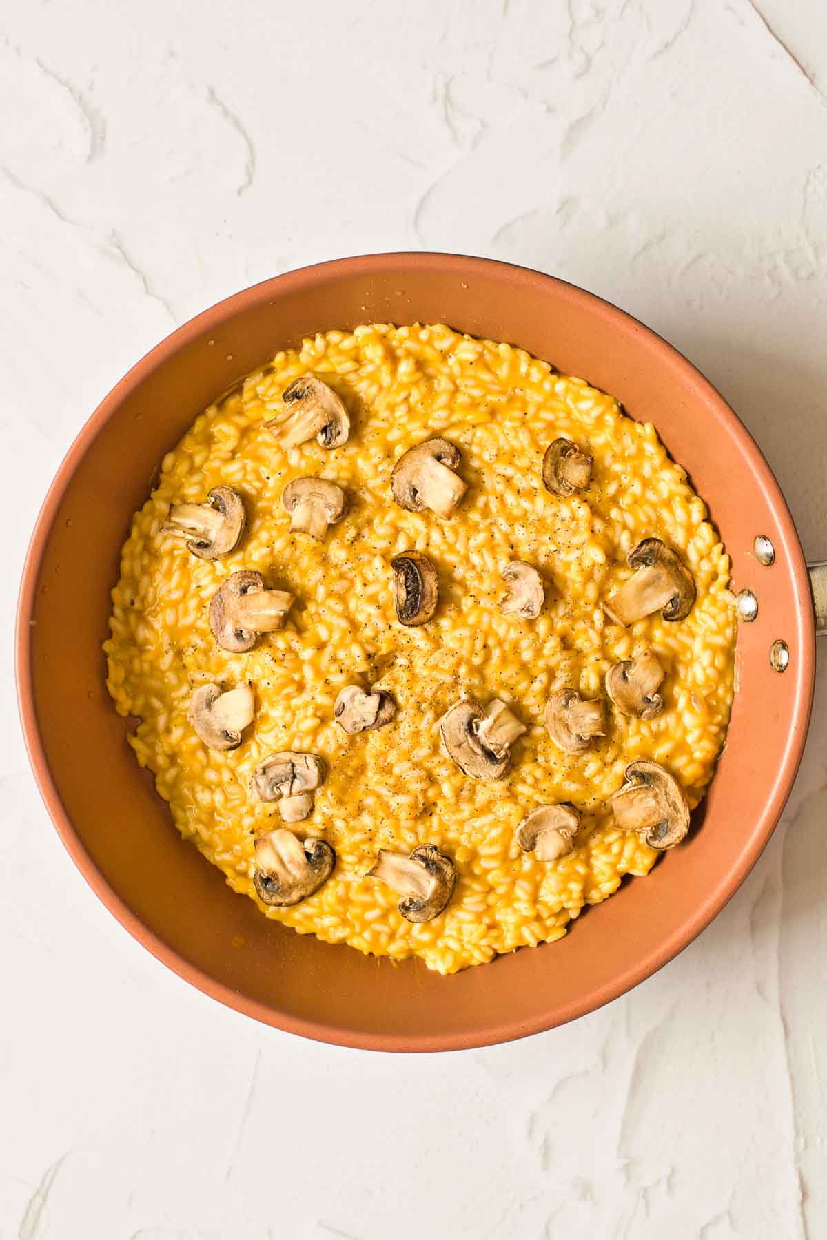 A big shallow bowl full of light-orange-colored pumpkin risotto. It is covered in sautéed mushrooms.