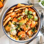 The finished curried chicken served in a bowl with bread and tahini dressing drizzled on top.