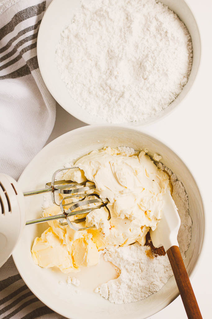 Powdered sugar added to a white bowl with cream cheese and other ingredients.