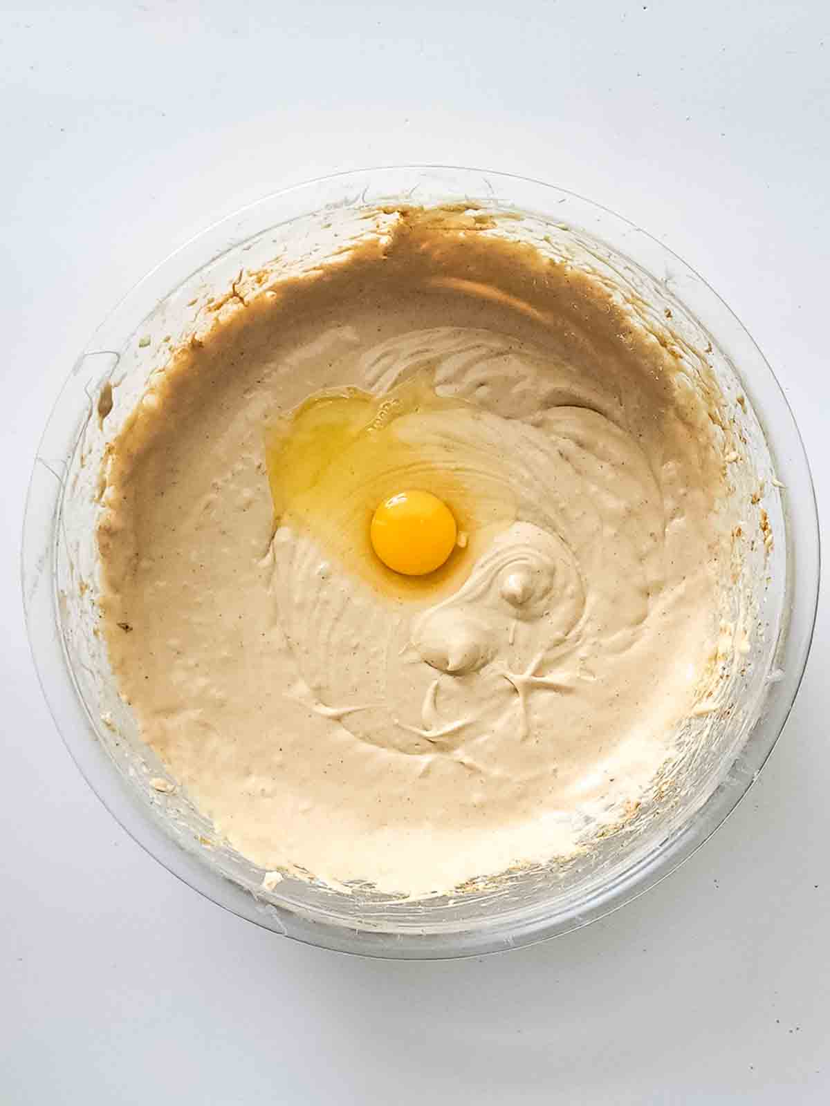 Ann egg cracked into the cheesecake filling in a glass bowl.