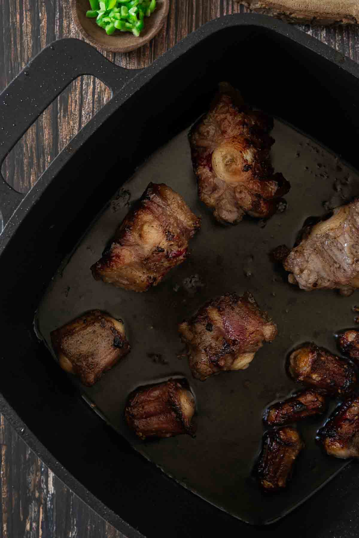 Oxtail pieces browning in hot fat in a heavy black cas iron pan.
