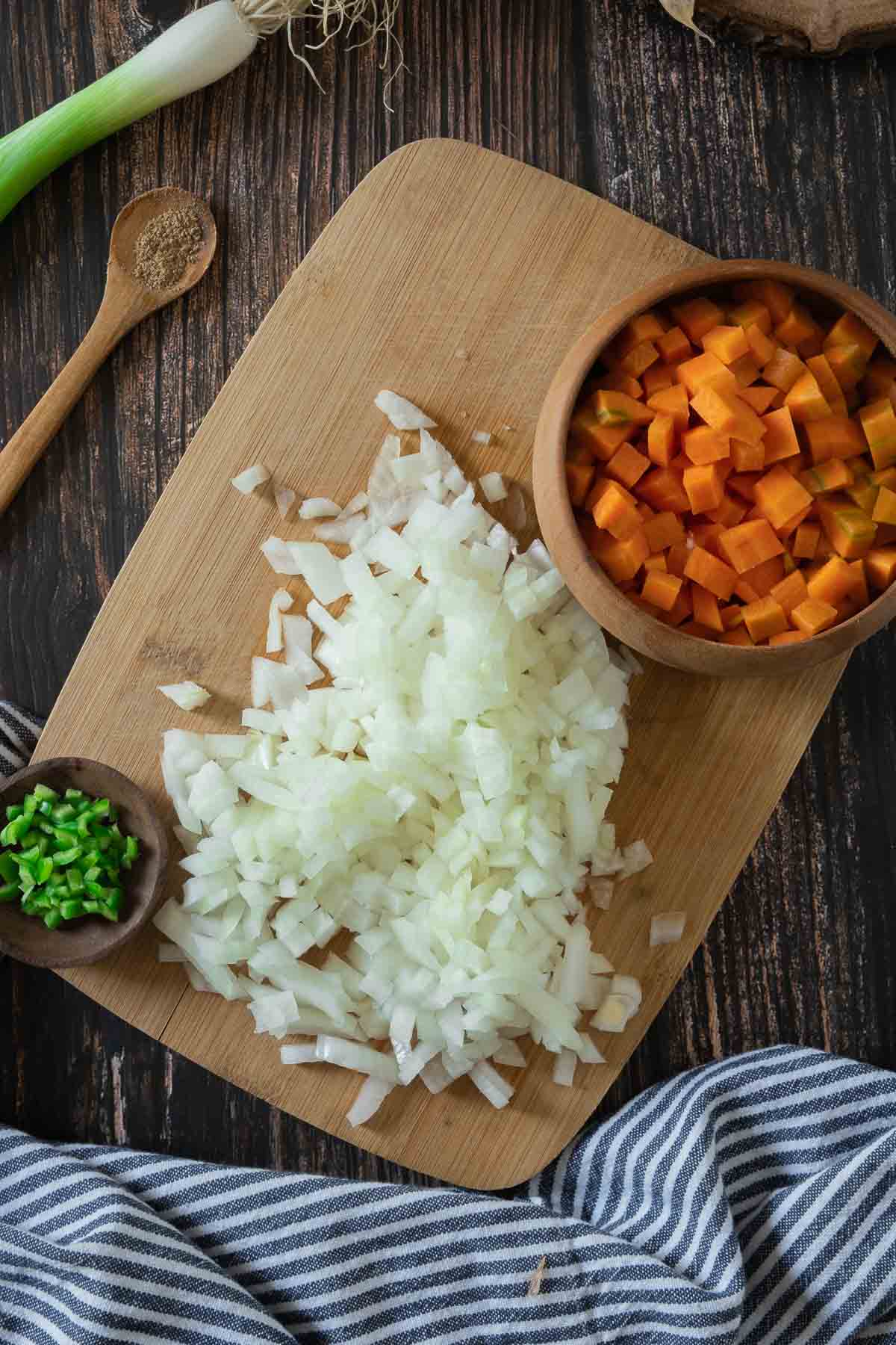 Diced and minced vegetables and aromatics on a wooden board.