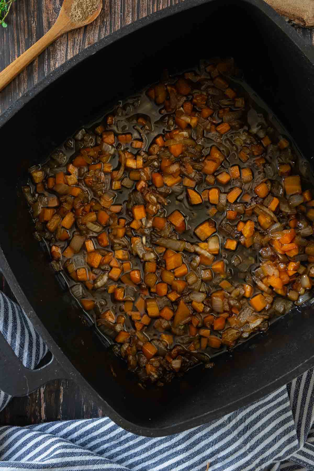 Vegetables and aromatics being browned in a heavy black cast iron pot.
