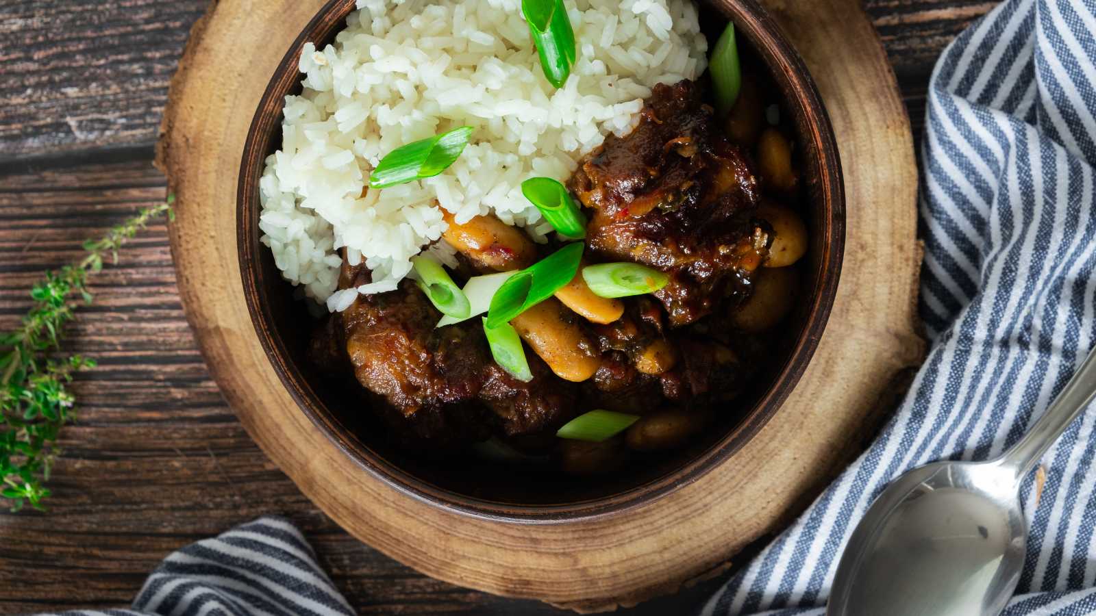 A bowl of thick Jamaican oxtail stew next to white rice.