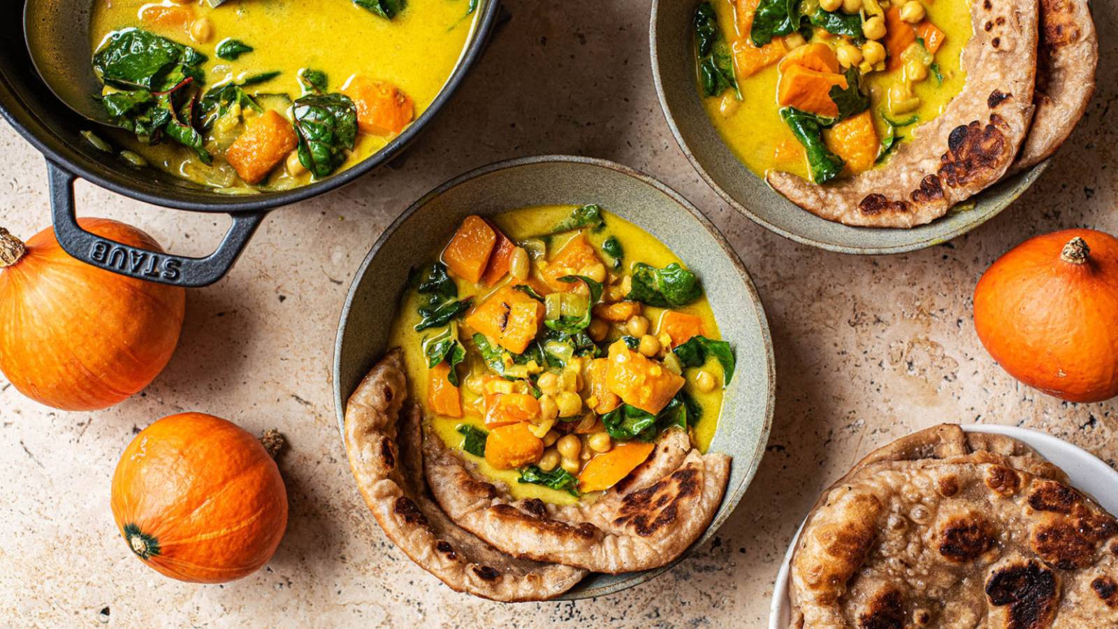 Two bowls of pumpkin curry with chunks of veggies served in bowls with naan.