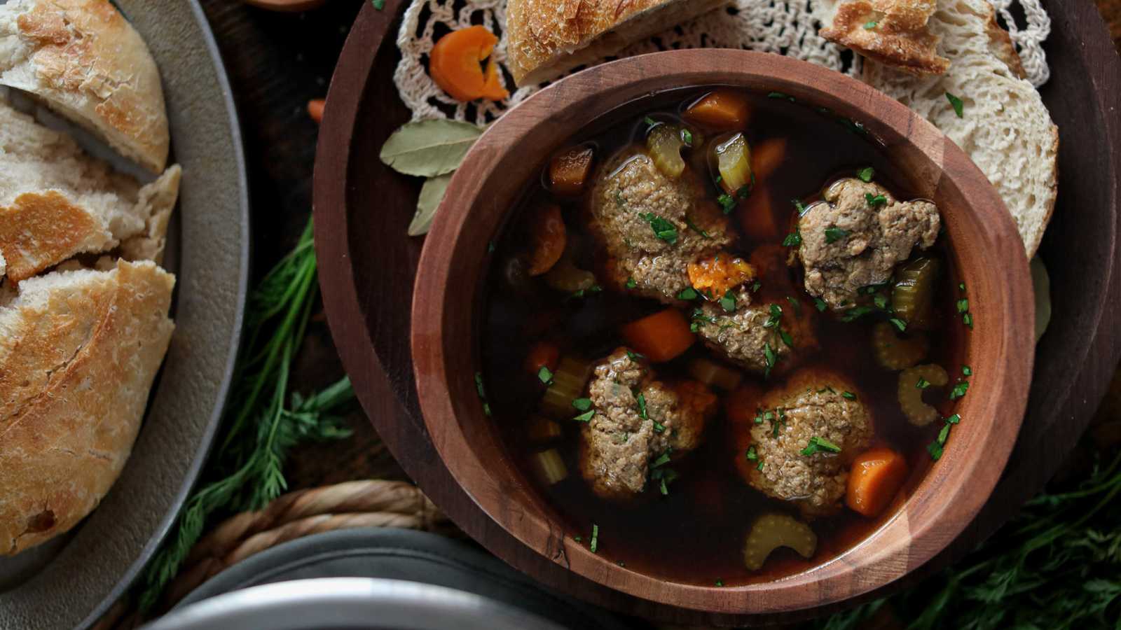 A wooden bowl full of liver dumplings floating in a beef based broth with vegetables.