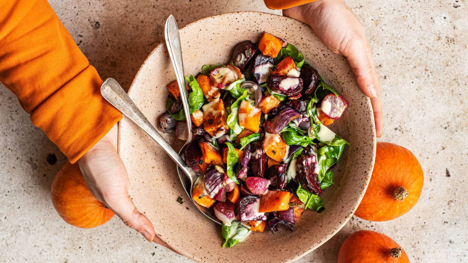 Two hands cradle a bowl full of roasted pumpkin and beet salad.