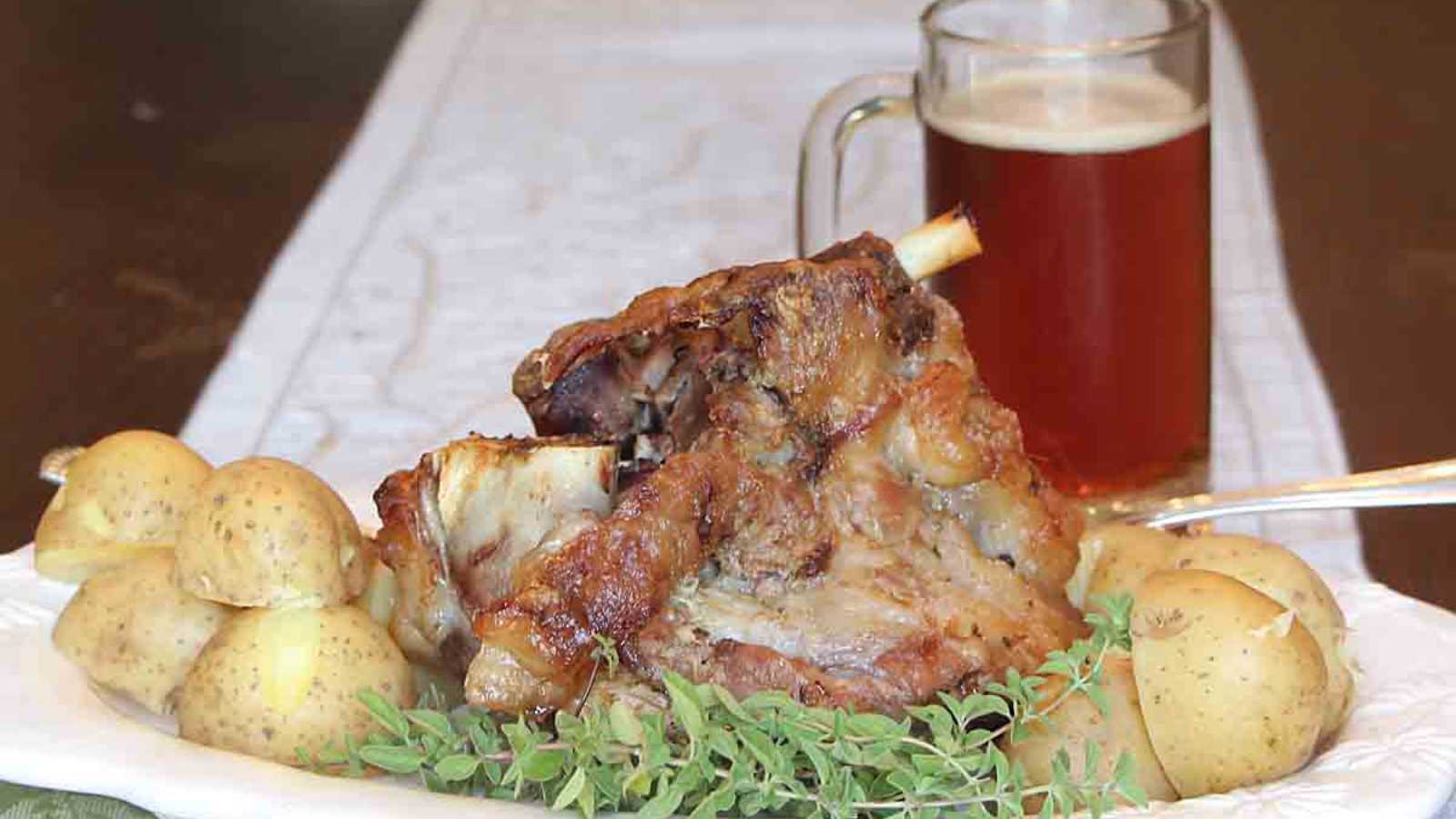 A plate of crispy pork hock and boiled potatoes, along with a pint of beer.