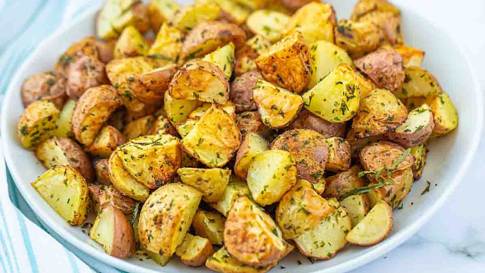 Roasting potatoes seasoned with herbs and spices in plate.