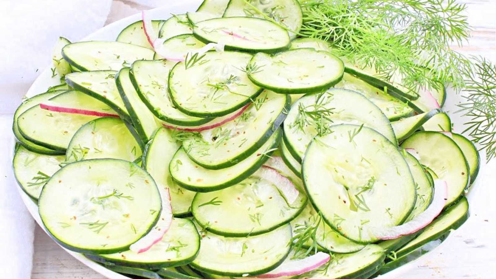 Thinly sliced cucumber in a bowl with red onion and herbs.