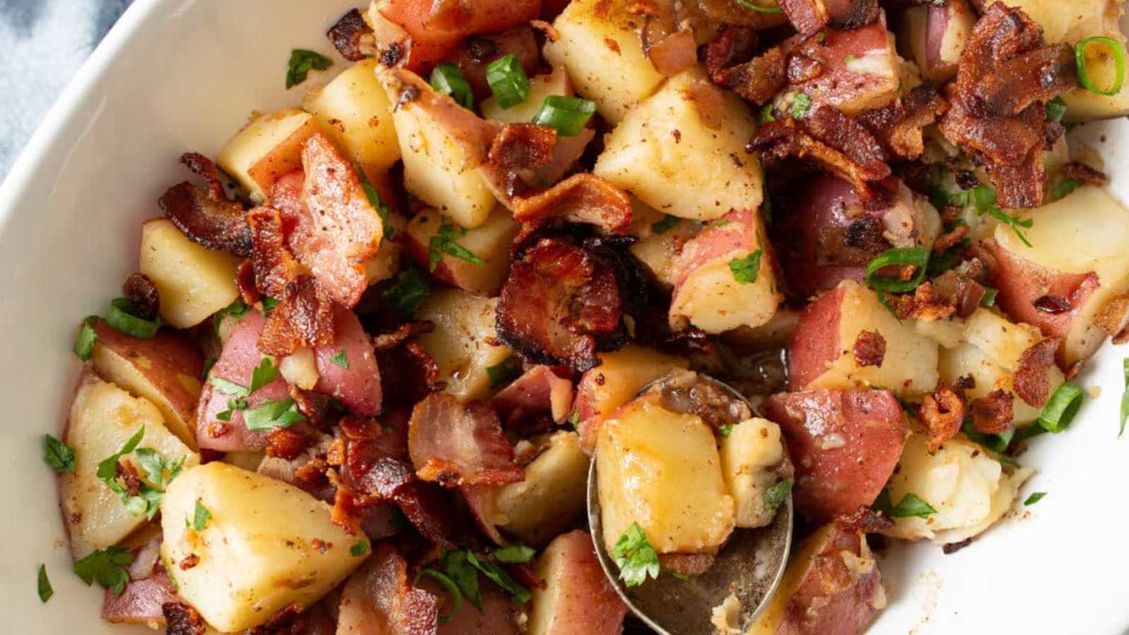 German potato salad featuring red potatoes, purple onions, and bacon in a white bowl.