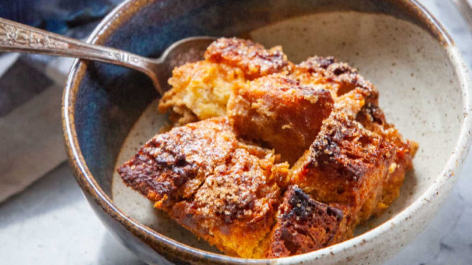 A bowl of pumpkin bread pudding elevated with the richness of brown butter and the sweet, tart notes of dried cranberries.