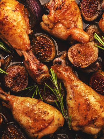 Baked chicken legs, drumsticks with sweet figs and red onions in balsamic marinade on baking sheet, close up, top view