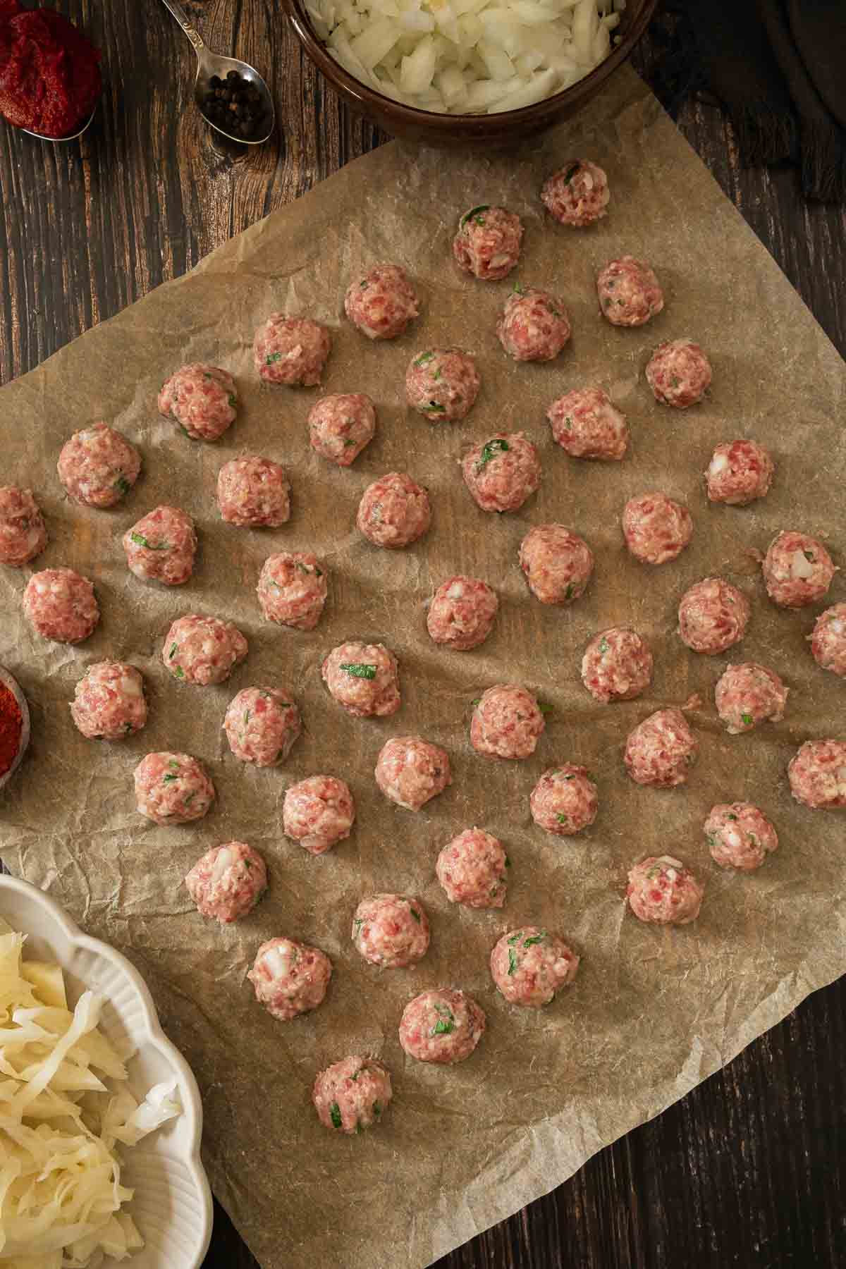 A sheet of parchment paper covered in small meatballs.