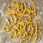 The finished homemade egg noodles on a floured sheet of parchment paper.