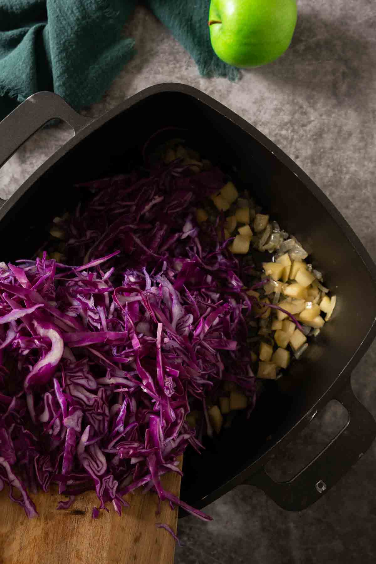 Shredded red cabbage being added to veggies in black pot.