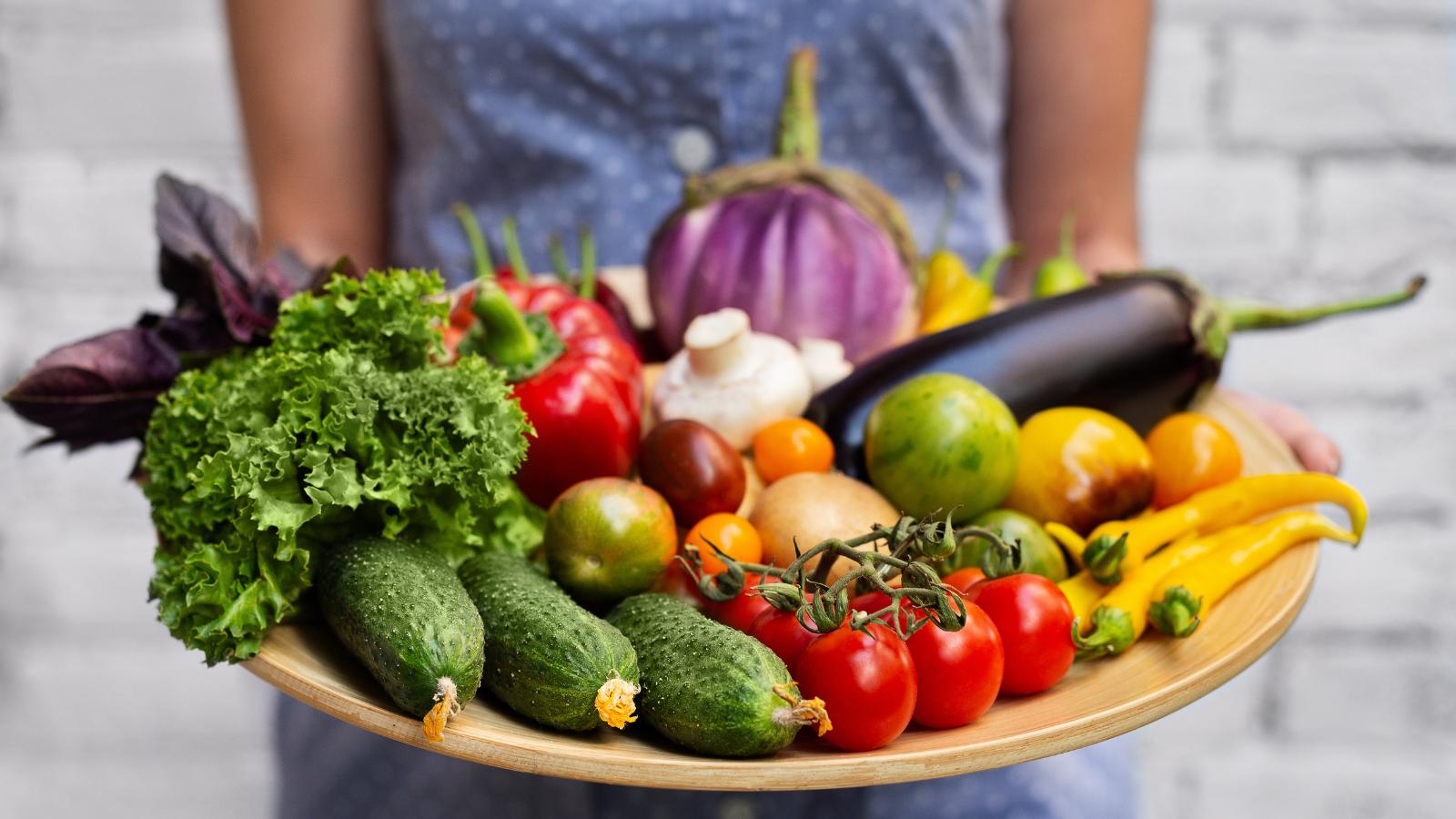 Woman holding platter of fresh garden veggies.
